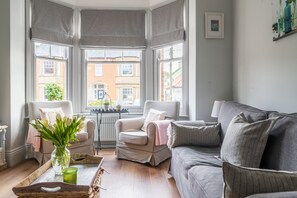 A cozy living room with a grey sofa, a wicker chair, and a small table with a vase of flowers. - Danes House (4), Aldeburgh (Aldeburgh)