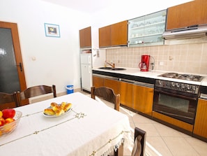 A kitchen with wooden cabinets, a white countertop, a red coffee maker, and a dining table with a fruit bowl. - Apartment 926 by Interhome (Bokordici)