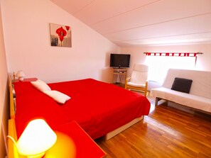A hotel room with a red bed, a white sofa, a television, and a painting on the wall. - Apartment 994 by Interhome (Fažana)