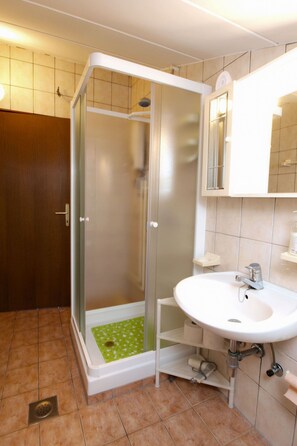 Ein Badezimmer mit Duschkabine, einem weißen Waschbecken und einem Spiegel darüber.