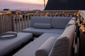 A rooftop deck with a white sofa, a small table, and string lights.