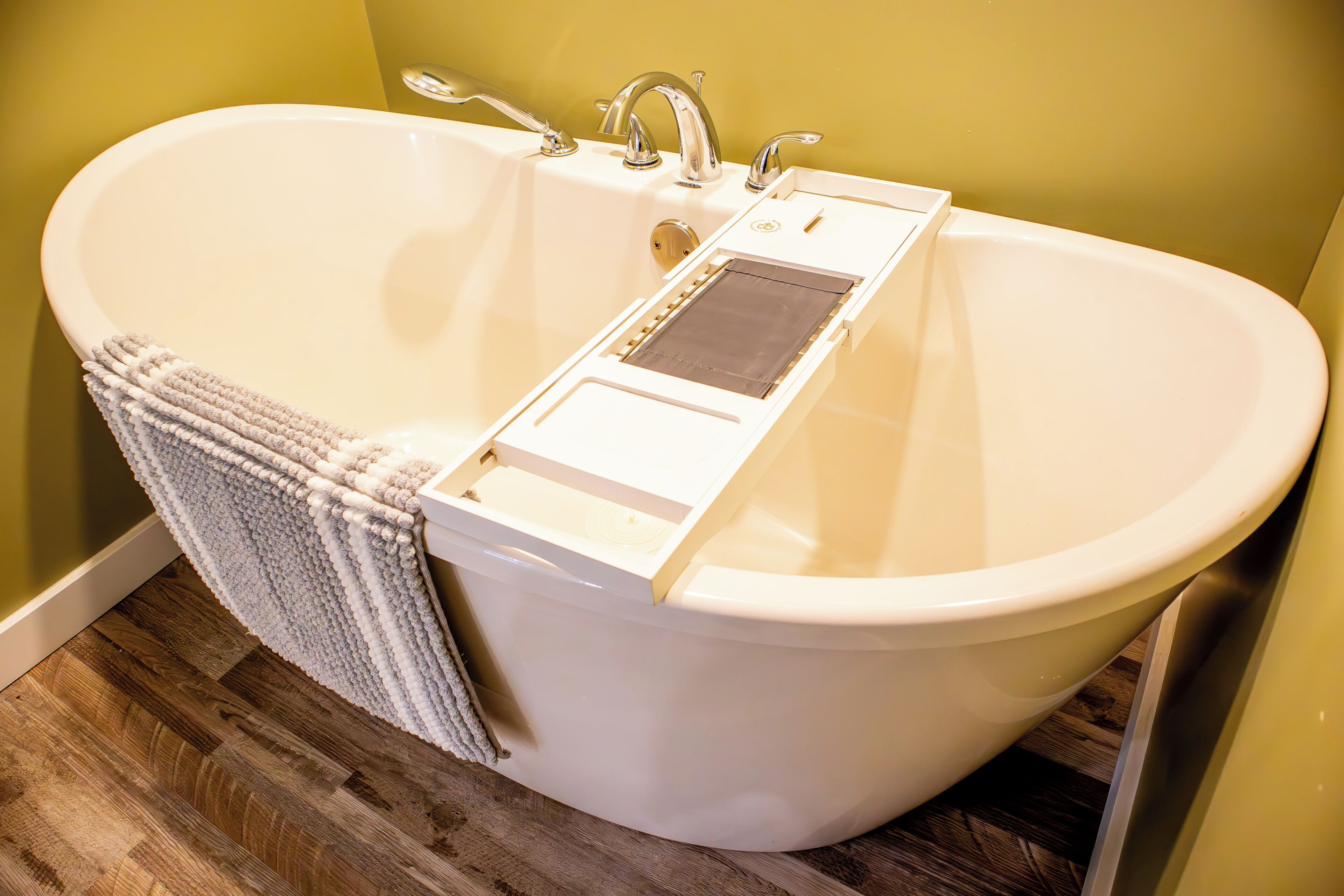 Une baignoire blanche, autoportante, dotée d’un panneau de douche intégré, d’un porte-serviettes et d’un plancher en bois.