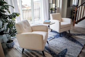 A living room with two white armchairs, a potted plant, and a rug.