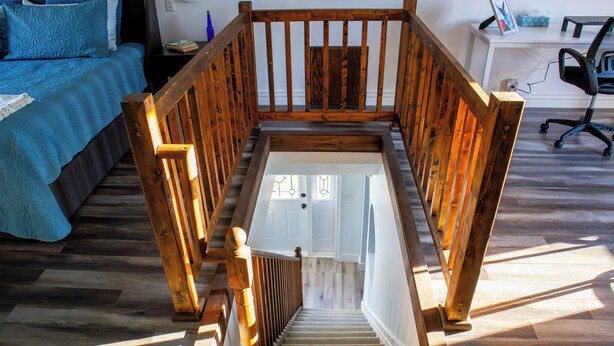 Un escalier avec des rampes en bois menant à une pièce où se trouvent un lit et un bureau.