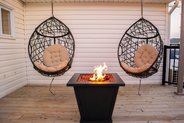 A patio with two hanging chairs and a central fire feature.