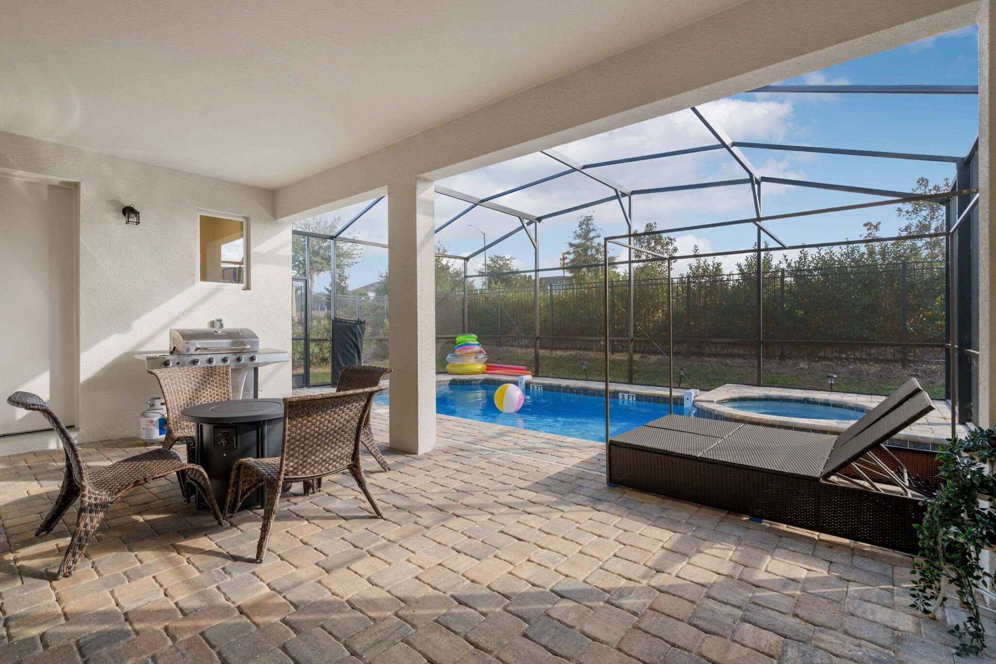 An outdoor patio with a grill, seating, and a view of a swimming pool and hot tub.