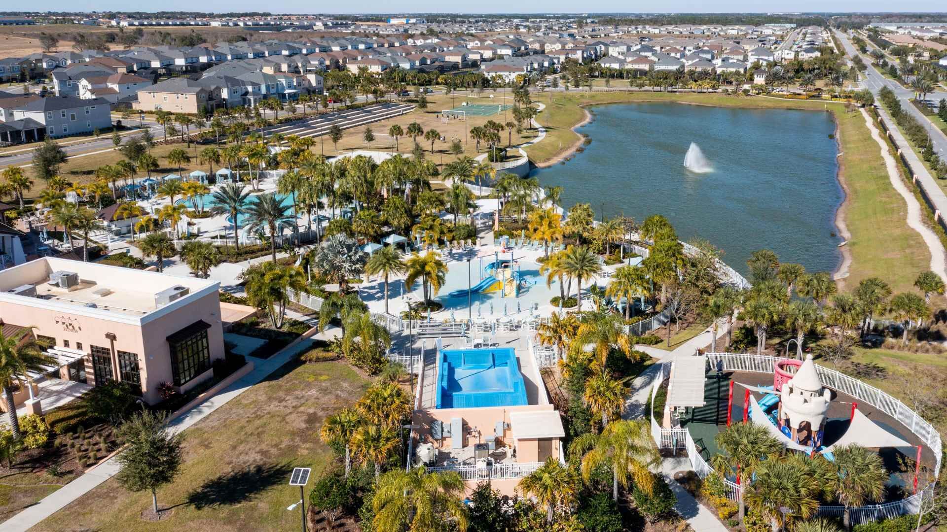 A residential area with a large swimming pool, palm trees, and a lake.