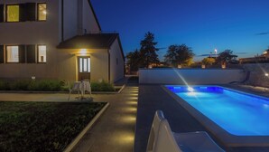 A modern house with a swimming pool, a patio with a table and chairs, and a well-lit entrance. - Villa Valbandon by Interhome (Fažana)