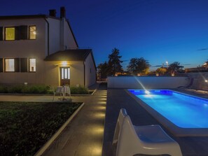 Ein modernes Haus mit Pool, einer Terrasse mit Tisch und Stühlen sowie einem gut beleuchteten Eingangsbereich.