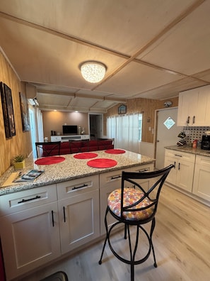Una cocina con una isla central, un comedor con sillas y un refrigerador.