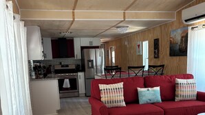 Um sofá vermelho com almofadas estampadas, uma cozinha com armários brancos e uma área de jantar com mesa e cadeiras.
