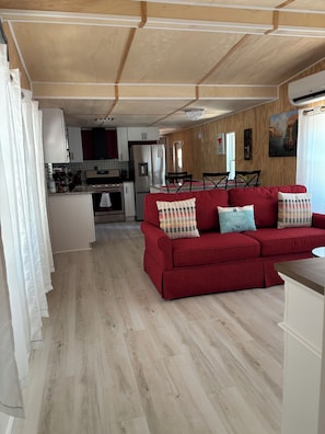 Un sofá rojo con cojines estampados, una cocina con armarios blancos y un comedor con mesa y sillas.