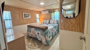 Quarto com uma cama, espelho, luminária e porta.