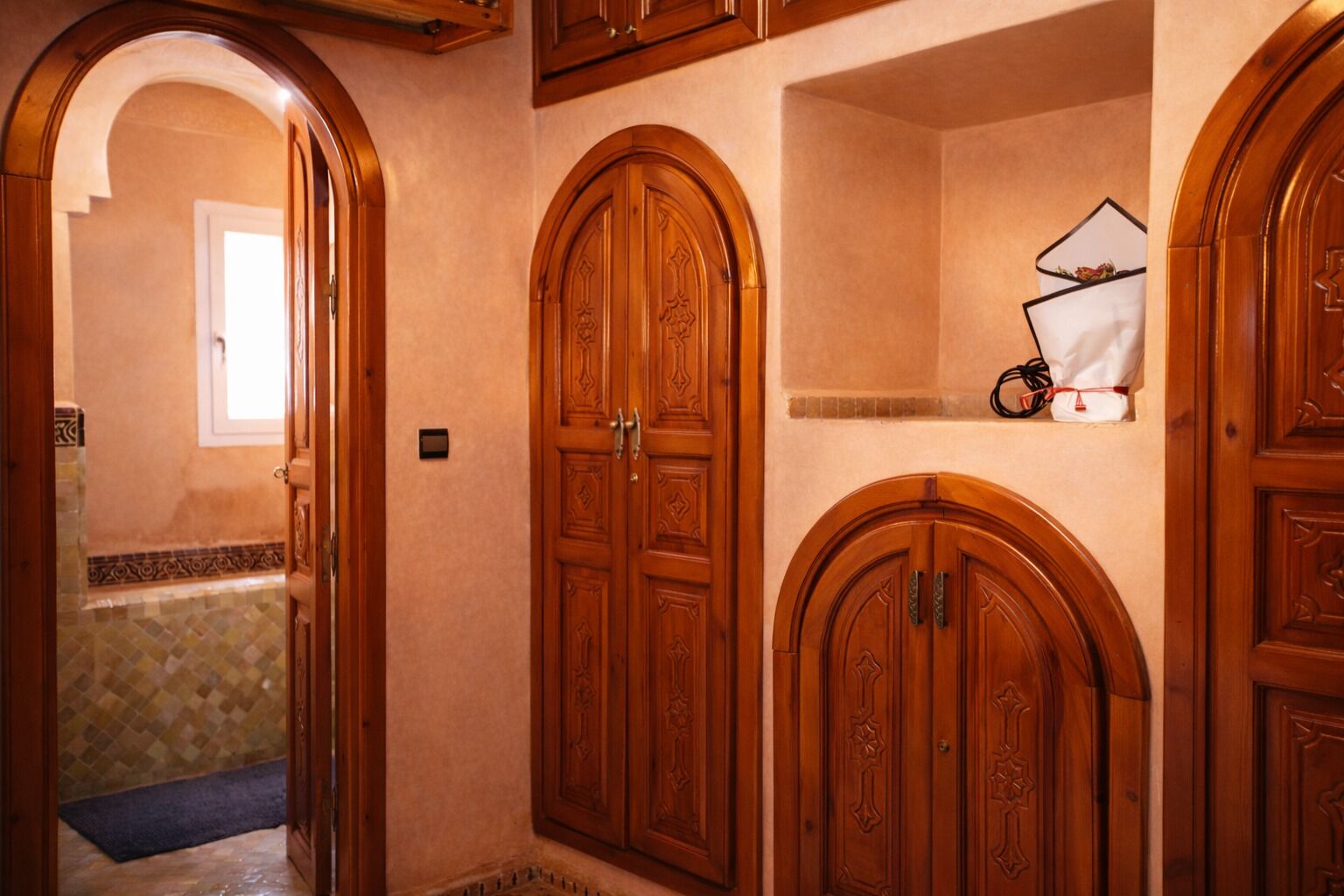 Un pasillo con puertas de madera, suelo de baldosas y un ventanal pequeño.