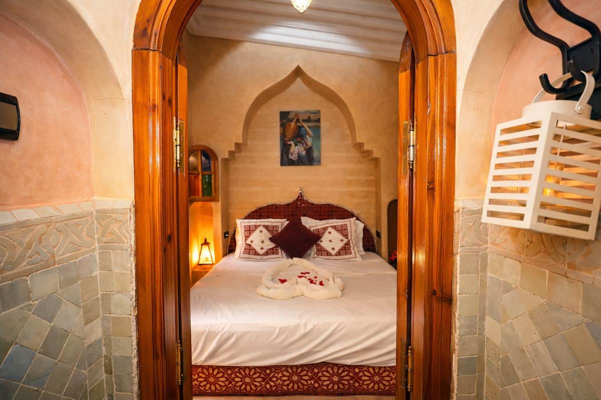 A room with a bed, a wooden door, a wall-mounted light fixture, and a patterned floor.