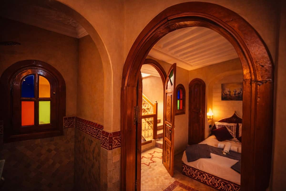 A room with a bed, a window with stained glass, and a staircase.