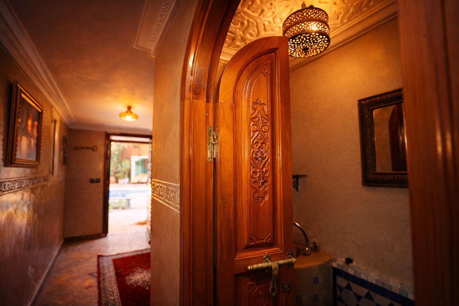 A hallway with a wooden door, a mirror, and a hanging light fixture.
