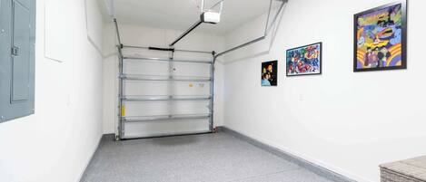 A clean, empty room with a grey floor, a metal-framed door, and two framed artworks on the wall.