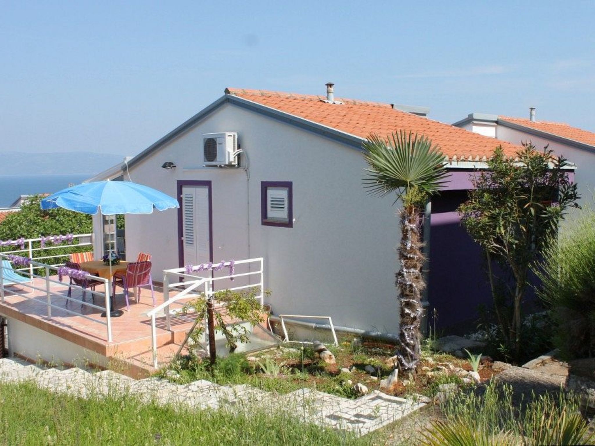 Een gebouw met een rood pannendak, een klein terrasje met een tafel en stoelen, en een palmboom.