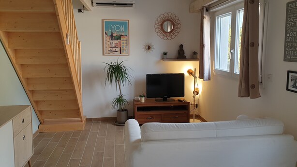 Ein Zimmer mit einer Holztreppe, einem Flachbildfernseher auf einem Holzboden, einem Blumentopf, einem wandmontierten Spiegel und einem Fenster mit Vorhängen.