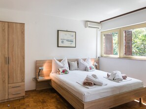 Ein Schlafzimmer mit einem Holzbett, weißer Bettwäsche, einem Nachttisch, einem Kleiderschrank, einem gerahmten Bild und einem Fenster mit Fensterläden.
