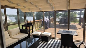 A covered outdoor seating area with a sofa, a table, and a grill. - Charming Waterfront Cottage –  Fully Equipped Kitchen & Fast Wi-Fi (Plaisance)