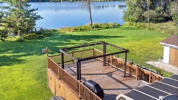 A wooden deck with a gazebo overlooking a lake, surrounded by greenery and a small shed. - Charming Waterfront Cottage –  Fully Equipped Kitchen & Fast Wi-Fi (Plaisance)