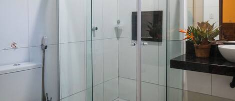 Un baño moderno con ducha de vidrio, inodoro y lavamanos con planta en maceta.