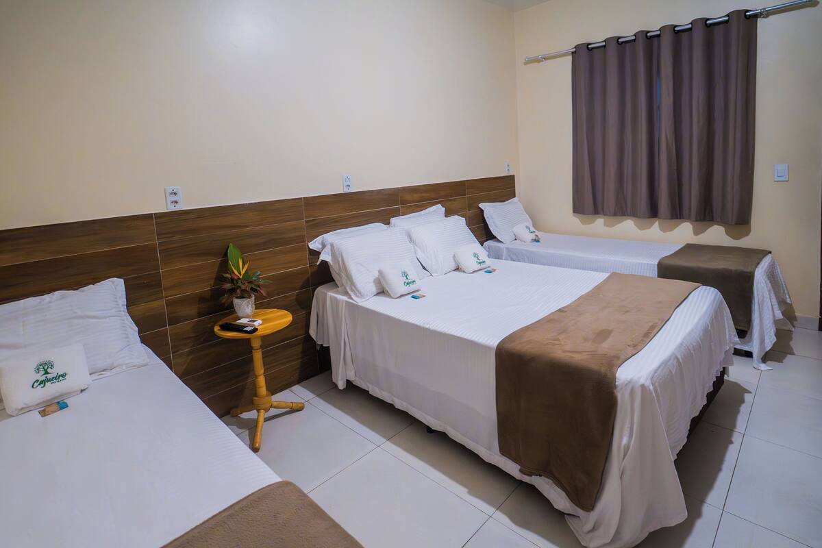 A hotel room with two beds, a wooden headboard, a small table with a plant, and a curtain.