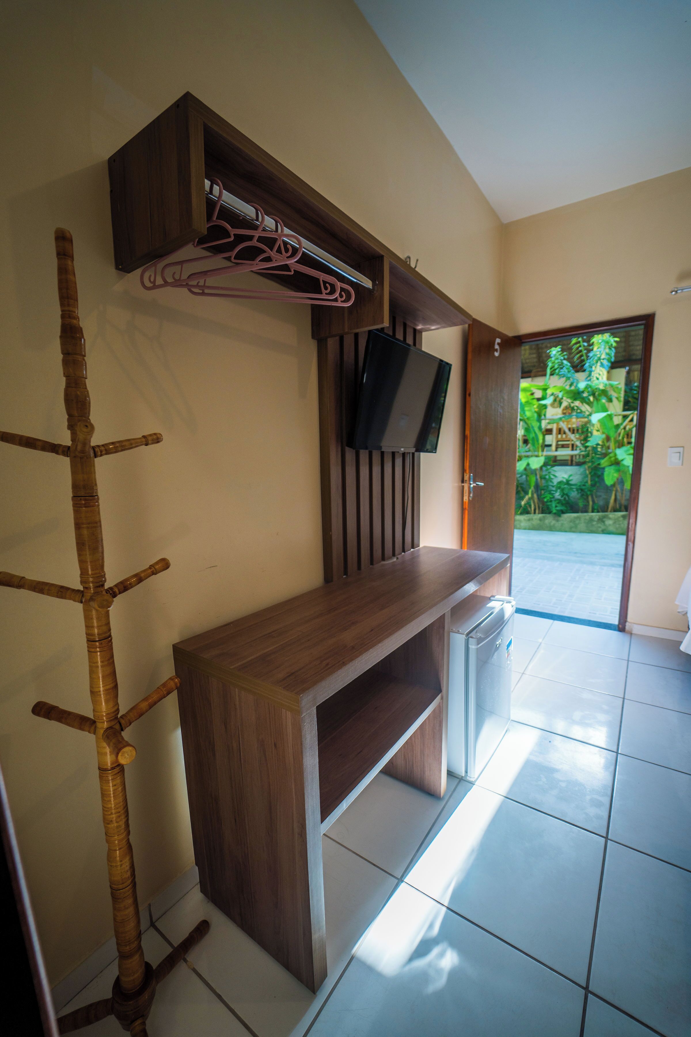 Un baño con tocador de madera, un organizador de bambú para la ducha, un televisor montado en la pared y una puerta que da a un jardín.