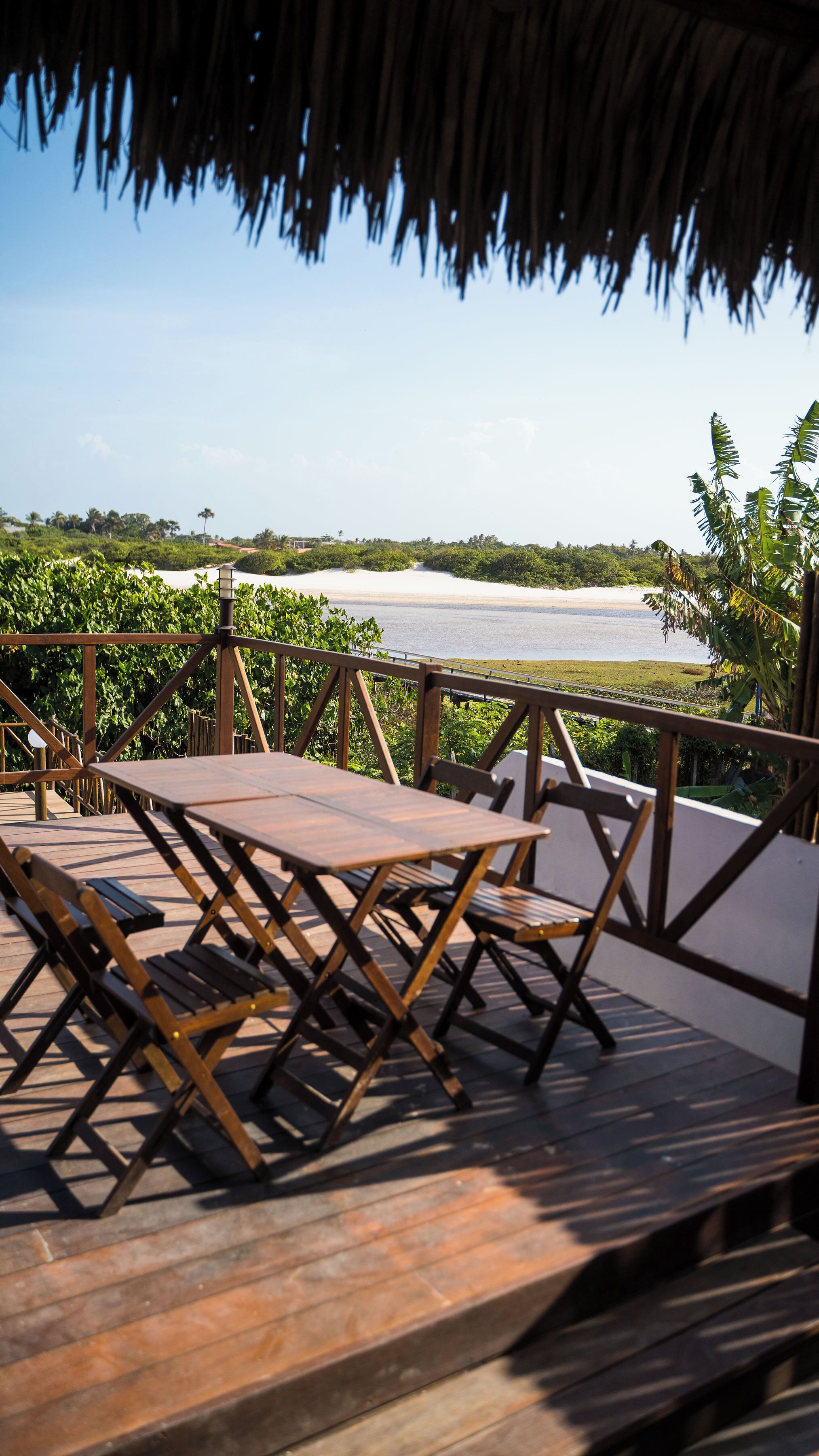 Um deck de madeira com mesa e cadeiras, com vista para uma praia e o mar.