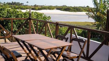 Um deck de madeira com mesa e cadeiras, com vista para uma praia e o mar.