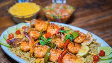 Een bord garnalen en groenten met rijst, limoenpartjes en een bakje salsa.