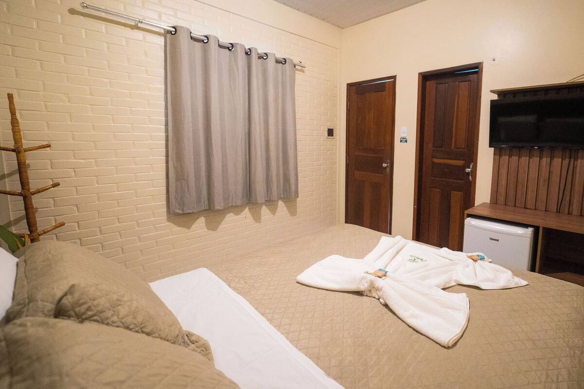 A hotel room with a bed, a wooden wardrobe, a small refrigerator, and a television on a wooden stand.