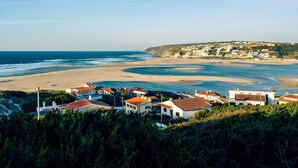 Uma cidade costeira com edifícios brancos e telhados vermelhos, uma praia arenosa e vista para o oceano.