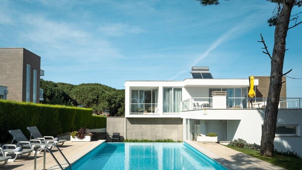 Uma casa moderna de dois andares com piscina, área de estar externa e vista para o verde ao redor.
