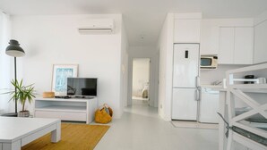 Um espaço de estar moderno e minimalista, com televisão de tela plana, uma pequena mesa, uma planta em vaso e um tapete amarelo.