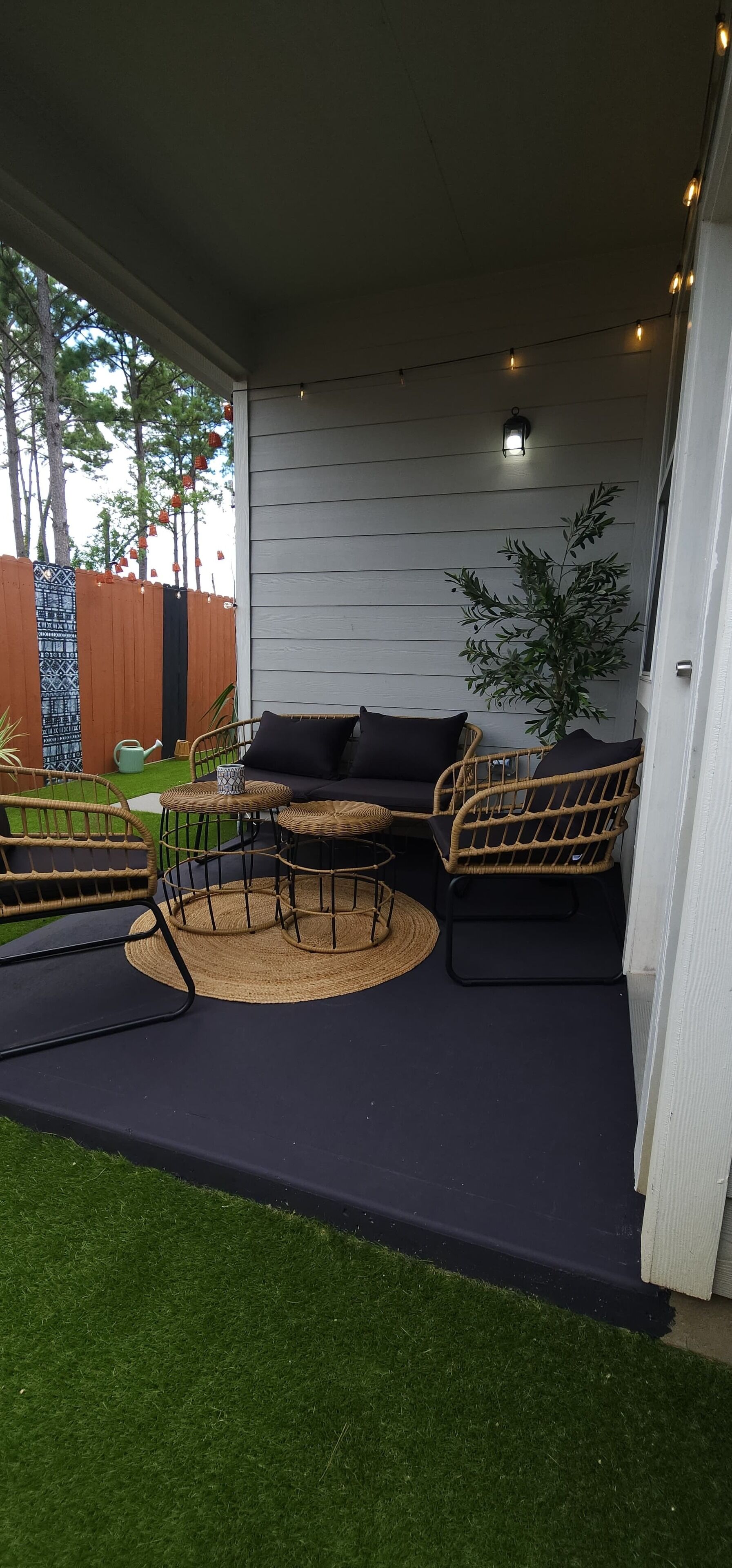 An outdoor patio with a black sofa, wicker chairs, and a small table.