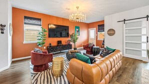 Un salon moderne avec un grand téléviseur, un canapé en cuir et un lustre.