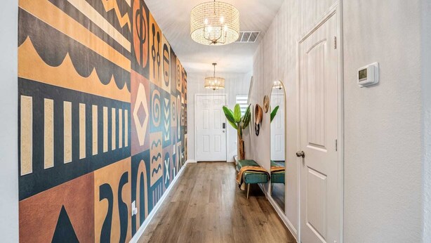 Un couloir aux murs ornés de motifs, doté d’un plancher en bois, d’un lustre et d’un banc agrémenté de plantes.