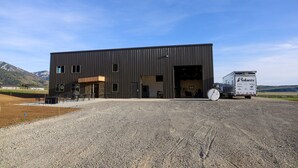 Un bâtiment industriel moderne doté d’une grande porte de garage à ouverture large, d’une allée gravillonnée et d’un camion garé.
