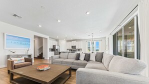 A modern living room with a grey sofa, a coffee table, and a bookshelf. - 5BR - Gorgeous Pool Home - Resort Close To Disney (Kissimmee)