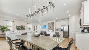 A modern kitchen with white cabinets, a stainless steel refrigerator, and a wooden dining table with black chairs. - 5BR - Gorgeous Pool Home - Resort Close To Disney (Kissimmee)