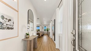 A hallway with a wooden floor, a console table with a potted plant, a framed picture, and a door with a glass panel. - 5BR - Gorgeous Pool Home - Resort Close To Disney (Kissimmee)