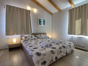 A bedroom with a bed, curtains, a nightstand, a wall-mounted light, and a framed picture. - Villa Mugeba I by Interhome (Dracevac)