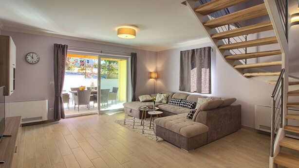 A modern living room with a sofa, a coffee table, a staircase, and a view through a glass door. - Villa Mugeba I by Interhome (Dracevac)