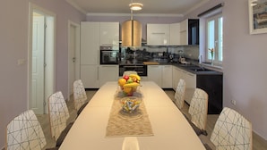 A modern kitchen with white cabinets, a central island with fruit, and a pendant light. - Villa Mugeba I by Interhome (Dracevac)
