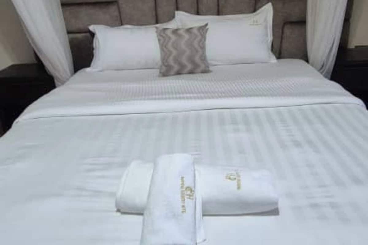A neatly made bed with white linens and two towels, a grey pillow, and a headboard.