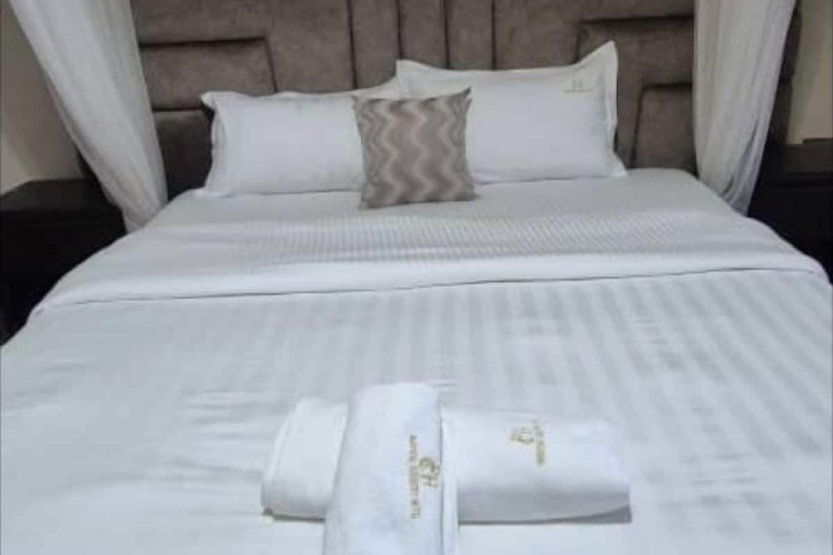 A neatly made bed with white linens and two towels, a headboard, and a nightstand with a lamp.