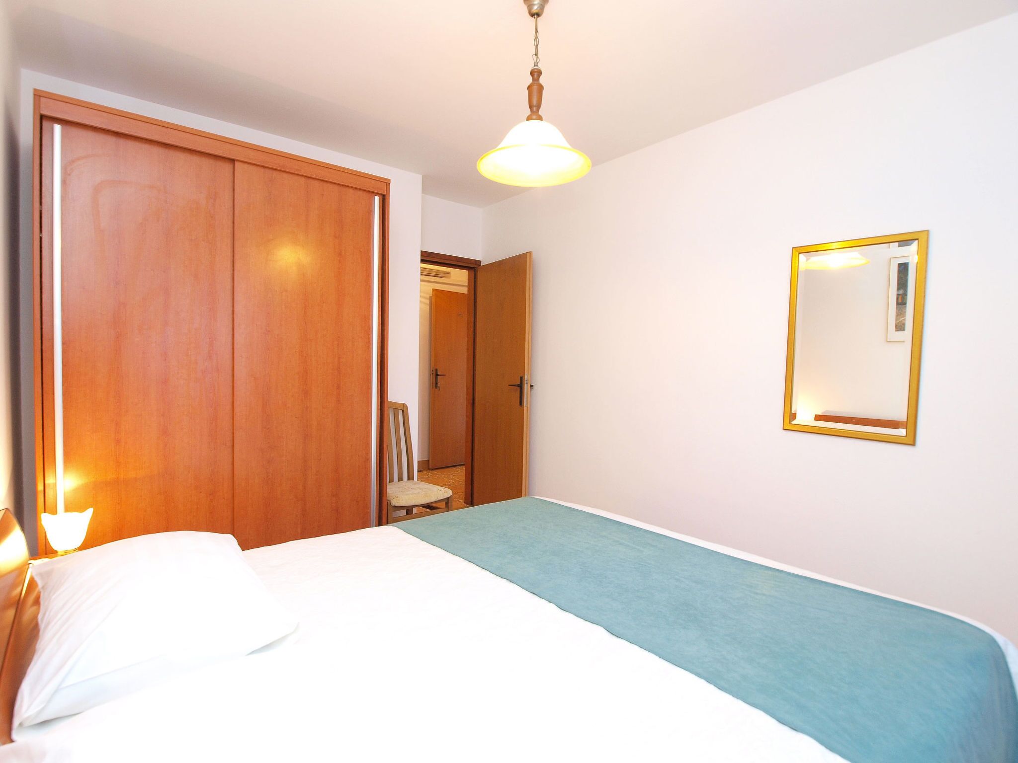 A bedroom with a bed, a wooden wardrobe, a mirror, and a ceiling light.